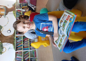 Chłopiec uśmiecha się do zdjęcia. Na kolanach trzyma książkę